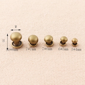 May include: Five different sizes of round, gold-toned metal rivets. The rivets are arranged in a row from largest to smallest. The measurements of each rivet are labeled below: 10*8mm, 7*7mm, 7*6mm, 6*5mm, 5*4mm.