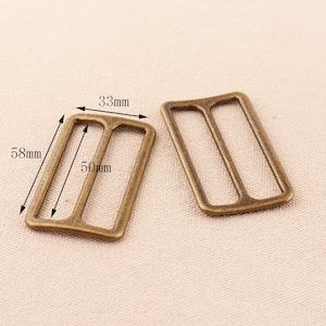 Könnte beinhalten: Zwei antike goldfarbene Metall-Schiebeschließen, eine mit den Maßen 33 mm x 58 mm und die andere mit 50 mm x 33 mm.