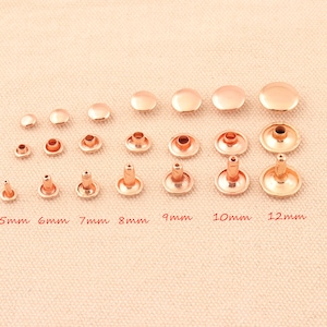 May include: Assortment of rose gold metal rivets in various sizes, ranging from 5mm to 12mm. The rivets are arranged in rows by size, with the smallest on the left and the largest on the right.