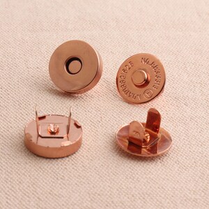 May include: Four copper-coloured magnetic snaps. Two snaps have a flat back and two snaps have a back with two prongs. One snap has the text "AOMID 888828 NO.985313" engraved on the front.