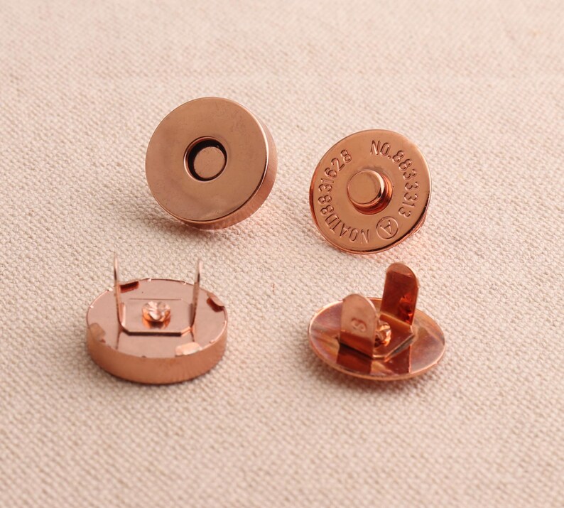 May include: Four copper-coloured magnetic snaps. Two snaps have a flat back and two snaps have a back with two prongs. One snap has the text "AOMID 888828 NO.985313" engraved on the front.