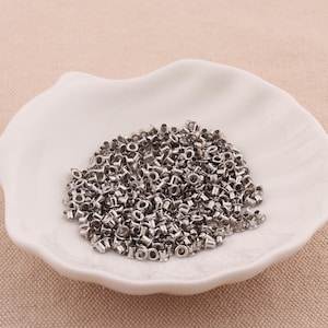 Könnte beinhalten: Eine weiße Keramikschale gefüllt mit einer großen Menge silberner Metallösen. Die Ösen sind klein, rund und haben ein Loch in der Mitte.
