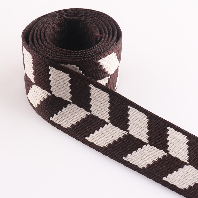 May include: Brown and white striped webbing with a checkered pattern. The webbing is rolled up and the stripes are running vertically.