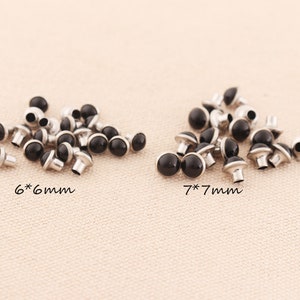 May include: Black and silver metal studs in two sizes, 6 mm and 7 mm. The studs are arranged in two groups on a light beige surface.