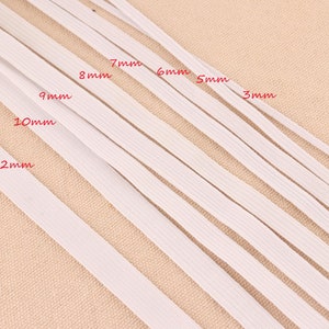 May include: White elastic bands of varying widths, labeled from 3mm to 12mm. The bands are arranged diagonally across the frame, showcasing the different sizes available. The background is a neutral beige color.