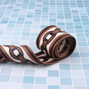 May include: Brown and white patterned fabric ribbon with a chain link design. The ribbon is rolled up and the fabric is textured.