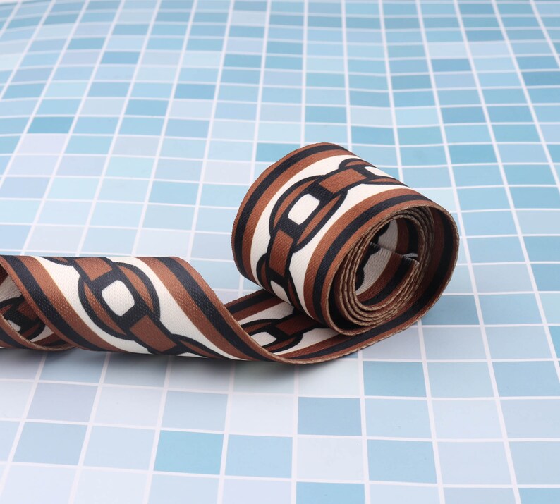 May include: Brown and white patterned fabric ribbon with a chain link design. The ribbon is rolled up and the fabric is textured.