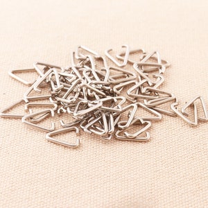 May include: A pile of silver triangle-shaped metal rings. These rings are used for attaching straps or other materials to fabric.