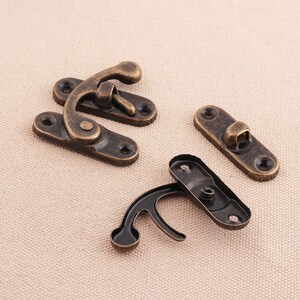 May include: Four antique bronze-colored metal latches. Two are assembled, and two are disassembled. Each latch has a curved hook and a rectangular base with screw holes. The metal has a distressed finish.