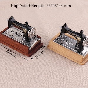 May include: Two miniature black sewing machines with gold accents on wooden bases. The sewing machines are 33 mm high, 25 mm wide, and 44 mm long.