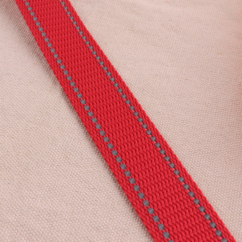 May include: Red webbing with a gray reflective trim. The webbing is woven and has a textured surface.