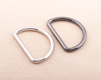 May include: Two metal D-rings, one silver and one black, on a light brown fabric background.