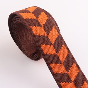 May include: Brown and orange woven webbing with a repeating pattern of orange arrows. The webbing is rolled up and ready to be used for crafting projects.