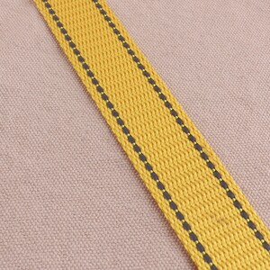 May include: A yellow fabric strap with black stitching. The strap is woven and has a textured surface.