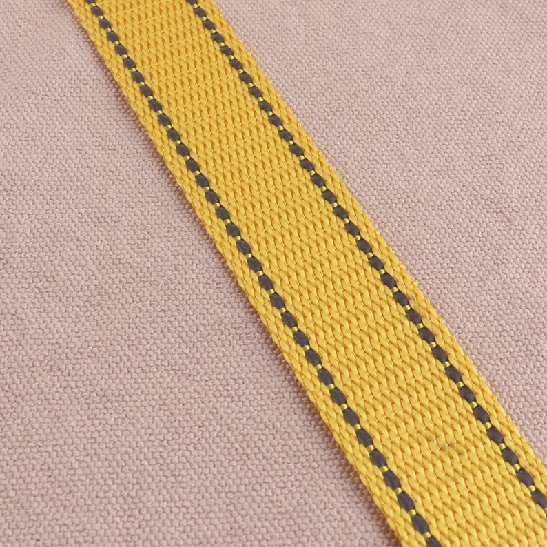 May include: A yellow fabric strap with black stitching. The strap is woven and has a textured surface.