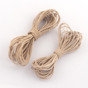 May include: Two bundles of natural-colored twine, tightly wound and tied. The twine is a light brown color, and the bundles are arranged on a white background. The twine appears to be made of a natural fiber.