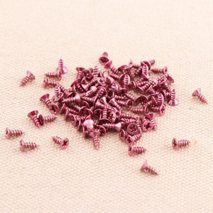 Pode incluir: Um monte de pequenos parafusos cor-de-rosa sobre uma superfície de tecido bege.