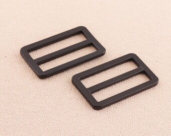 May include: Two black metal slider buckles. The buckles are rectangular with two parallel slots in the centre.