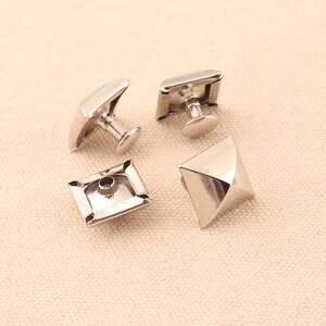 May include: Four silver pyramid-shaped studs with a square base. Two of the studs have a post on the bottom for attaching to fabric.