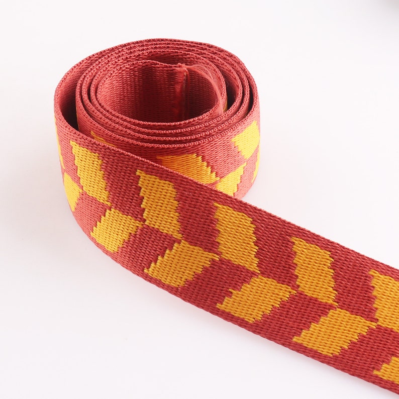 May include: Red and yellow woven webbing with a checkered pattern. The webbing is rolled up and the yellow squares are visible.