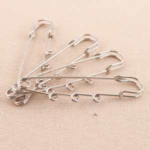 May include: Five silver safety pins with a decorative loop at the end of each pin.