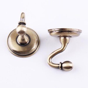 May include: Two antique gold-toned hooks with a round base and a curved hook. The hooks are made of metal and have a decorative design.