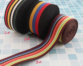 Pode incluir: Três rolos de fita de tecido listrada colorida. A fita é preta com listras brancas, amarelas, vermelhas, azuis, verdes, laranja e marrons. A fita está enrolada e as pontas são visíveis. Os rolos são etiquetados com 1#, 2# e 3#.