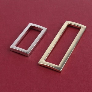 May include: Two metal belt buckle loops, one silver and one gold. The loops are rectangular with rounded corners and a slightly curved edge.