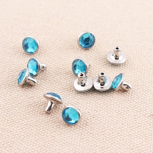 Puede incluir: Surtido de adornos de pedrería azul con engastes plateados. Algunos de los diamantes de imitación tienen un engaste de garras y otros tienen un dorso plano.