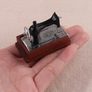 May include: A miniature black sewing machine with a wooden base. The machine has a silver metal plate with an ornate design.