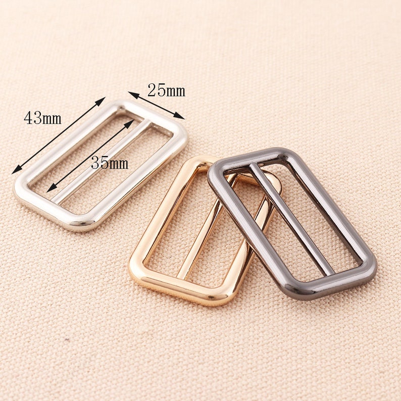 May include: Three metal belt buckle sliders in silver, gold, and black. The sliders are rectangular with rounded corners and measure 4.3 cm by 3.5 cm.