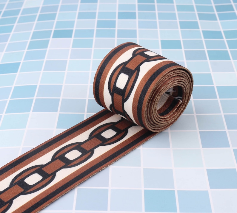 May include: Brown and white striped fabric ribbon with a chain link pattern. The ribbon is rolled up and the chain links are brown with white outlines.