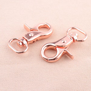May include: Two rose gold swivel clasps with a spring-loaded gate. The clasps are made of metal and have a shiny finish.