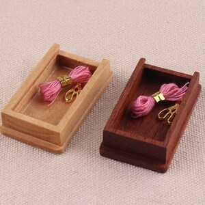 May include: Two wooden boxes with lids, one light brown and one dark brown, each containing a pink spool of thread and a pair of gold scissors.