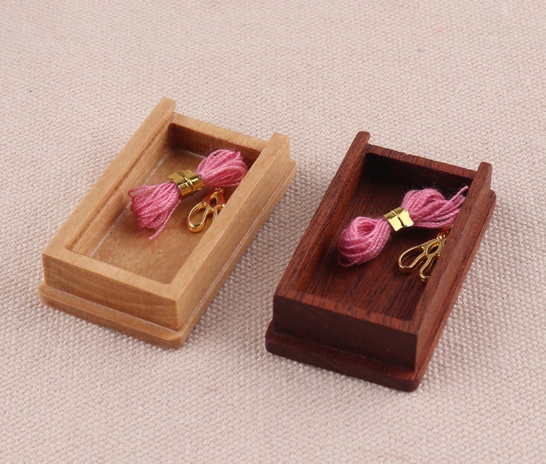 May include: Two wooden boxes with lids, one light brown and one dark brown, each containing a pink spool of thread and a pair of gold scissors.