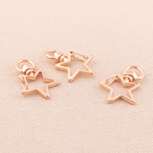 May include: Three rose gold star-shaped swivel clasps. Each clasp features a star outline with a ring and a lobster claw clasp. The clasps are designed for attaching to keychains, jewellery, or other accessories.