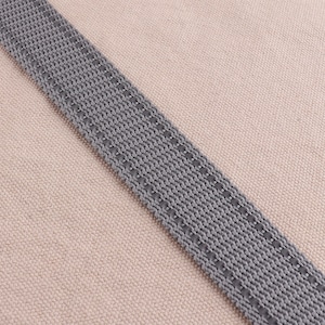 May include: A close-up of a gray woven strap with a stitched edge. The strap is on a light brown fabric background.