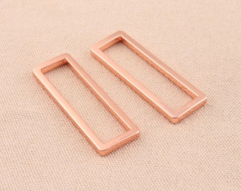 May include: Two rose gold metal rectangular frame shapes. The frames are open and have a smooth, polished finish.
