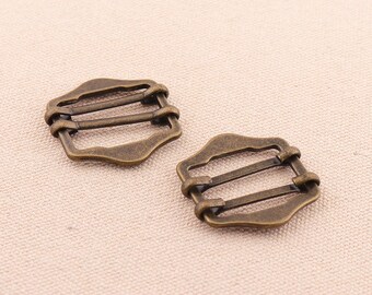 May include: Two antique gold-toned metal slider buckles with three slots. The buckles are rectangular with rounded corners and a decorative edge.