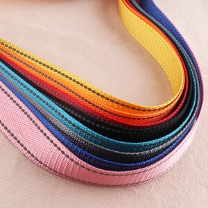 May include: A close-up of a multi-colored woven webbing with reflective stitching. The webbing is pink, blue, gray, black, teal, orange, yellow, and red.
