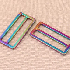 May include: Two iridescent metal slider buckles. The buckles are rectangular with a double-bar design. The metal has a rainbow finish.