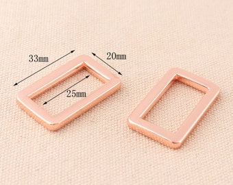 May include: Two rose gold metal rectangular rings with rounded corners. The rings are 33 mm long, 20 mm wide, and 25 mm in diameter.