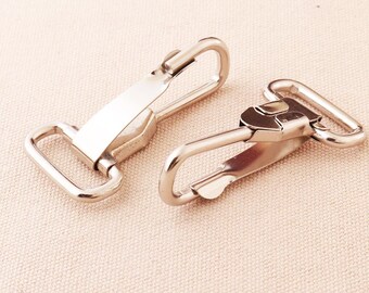 May include: Two silver metal swivel clasps, also known as trigger snaps, for attaching straps or leashes. The clasps are open and ready to be connected.