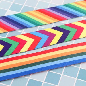 K&ouml;nnte beinhalten: Drei verschiedene Regenbogen-Bandborten. Die erste Borte hat ein Regenbogen-Streifenmuster. Die zweite Borte hat ein Chevron-Muster mit abwechselnden Regenbogenfarben. Die dritte Borte hat ein Regenbogen-Streifenmuster mit abwechselnden Farben.