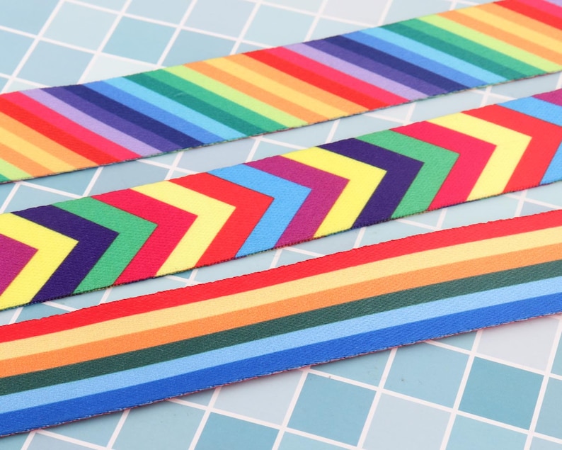 K&ouml;nnte beinhalten: Drei verschiedene Regenbogen-Bandborten. Die erste Borte hat ein Regenbogen-Streifenmuster. Die zweite Borte hat ein Chevron-Muster mit abwechselnden Regenbogenfarben. Die dritte Borte hat ein Regenbogen-Streifenmuster mit abwechselnden Farben.