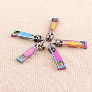May include: Five iridescent zipper pulls in a rainbow colour scheme. The pulls are made of metal and have a rectangular shape.