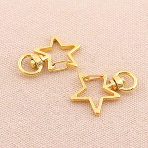May include: Two gold-toned star-shaped keyrings with a swivel clasp. Each keyring has a ring attached to the top.