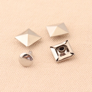 May include: Four silver metal pyramid-shaped studs with a flat base and a pointed top. One stud has a round post attached to the base.