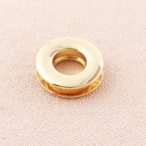 May include: Gold metal grommet with a round hole in the center. The grommet is designed for use with fabric or leather.