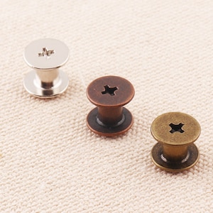 May include: Three metal screw-in button fasteners. One is silver, one is copper, and one is gold.